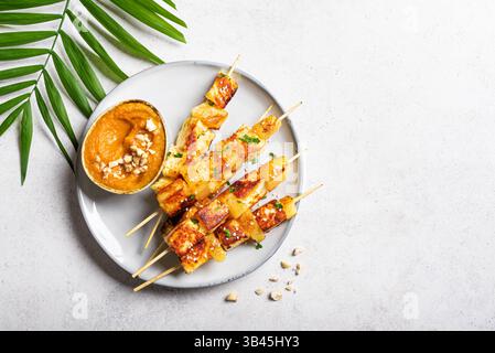 Brochettes satay de tofu grillé et d'ananas avec sauce aux arachides épicée sur fond blanc avec feuille de palmier, vue de dessus, espace de copie. Kebabs frits au fromage halloumi Banque D'Images
