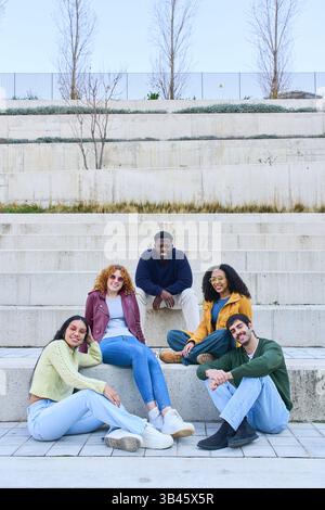 Cinq étudiants universitaires multiethniques se relaxant et souriant ensemble sur les escaliers du campus, profitant de leur temps dans une atmosphère vibrante et conviviale Banque D'Images