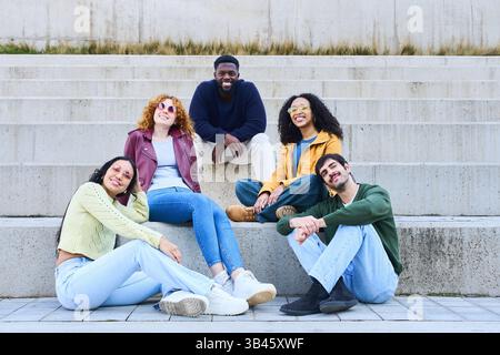 Groupe de jeunes personnes multiraciales profitant du temps ensemble à l'extérieur assis sur des gradins en béton Banque D'Images