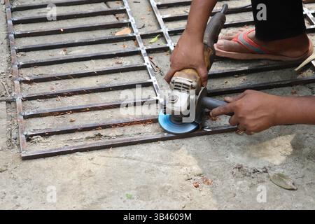 L'homme travaille à l'extérieur, en utilisant une meuleuse d'angle pour couper la grille métallique, étincelant. Concentré sur la main en utilisant l'outil électrique dans un vrai cadre extérieur. Banque D'Images