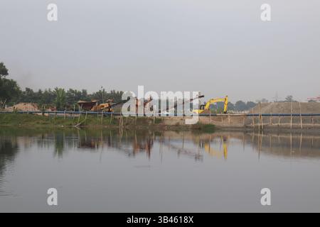 Le cliché présente de lourdes machines d'excavation près d'un lac, avec des reflets clairs visibles dans l'eau au milieu d'un paysage extérieur par une journée brumeuse. Banque D'Images