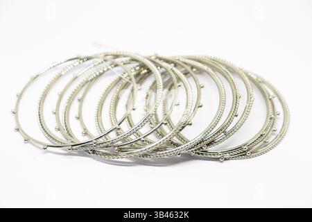 Gros plan capture une pile de bracelets argentés étincelants, mettant en valeur leurs motifs de perles détaillés sur un fond net et lumineux. Banque D'Images