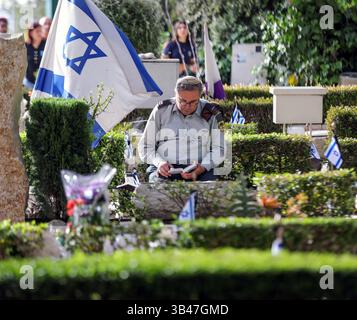 Jérusalem, Israël. 30 avril 2025. Israël commémore le jour du souvenir des soldats tombés au combat lors de cérémonies dans les cimetières militaires. Un officier assis à côté d'une tombe, priant. Derrière lui se trouve un grand drapeau israélien. Crédit : Yoram Biberman/Alamy Live News. Banque D'Images