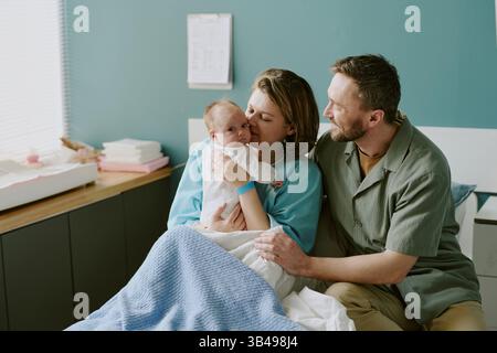 Parents tenant un nouveau-né en souriant dans une chambre d'hôpital. Bonheur et amour rayonnant du moment familial dans un environnement lumineux et paisible Banque D'Images