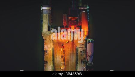 Ferry bateau amarré la nuit, voitures qui partent comme un coucher de soleil dramatique peint le ciel. Les lumières qui éclairent la scène se reflètent sur l'eau, créant une vue pittoresque sur la côte Banque D'Images