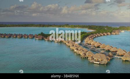 Bungalows sur l'eau hôtel de villégiature s'étendant sur un récif corallien atoll avec des palmiers et une plage privée, paradis tropical serein et idyllique. Nature sauvage éloignée, voyage exotique d'été. Prise de vue aérienne par drone Banque D'Images