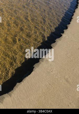 Des ondulations de sable à l'endroit où il rencontre l'eau ondulée sur une plage. Banque D'Images