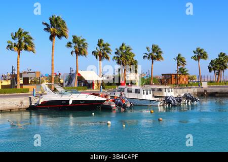 Yachts de luxe dans la marina à Hurghada, en Égypte, avec minarets mosquée et promenade bordée de palmiers sous un ciel bleu clair, scène de station balnéaire de la mer Rouge. Banque D'Images