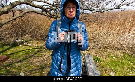 Une femme passionnée de plein air observe tranquillement à travers des jumelles dans un paysage rustique, embrassant le rythme des natures. Banque D'Images