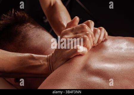 Gros plan de massage des tissus profonds sur le dos d'un homme, thérapeute appliquant une pression intense avec les mains serrées. Banque D'Images