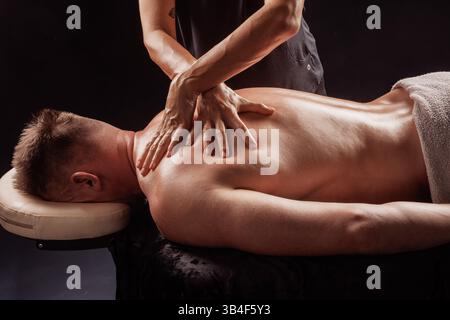 Gros plan du massage professionnel du dos des tissus profonds sur le client masculin dans le spa de bien-être, les mains appliquant une pression ferme. Banque D'Images