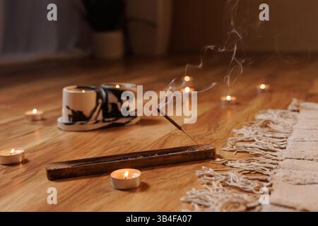 Gros plan de bâton d'encens brûlant avec des bougies sur plancher en bois, créant une atmosphère calme et méditative pour le yoga, la relaxation ou les pratiques de pleine conscience. Banque D'Images