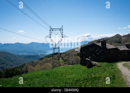 Une vue tranquille sur la montagne avec une cabine rustique et d'imposantes lignes électriques. Le lac et les collines lointaines offrent une toile de fond magnifique. Banque D'Images