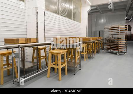 Nettoyer l'intérieur de la zone de travail de production alimentaire industrielle avec des rangées de tables en acier inoxydable, des tabourets en bois et des piles de plateaux Banque D'Images