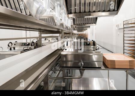 Vue rapprochée d'un équipement en acier inoxydable et d'une bande transporteuse dans une cuisine industrielle propre ou une chaîne de production de transformation des aliments Banque D'Images