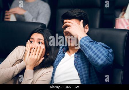Jeune homme avec sa petite amie qui fermait des visages dans la terreur tout en regardant un film d'horreur au cinéma Banque D'Images