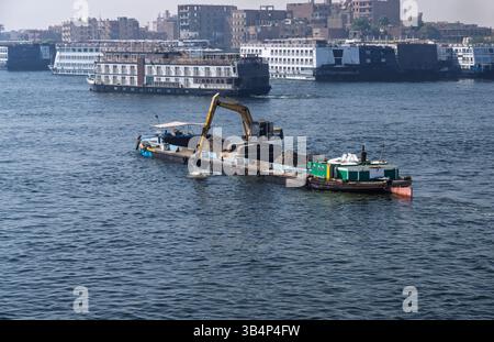 Port bondé à Edfou avec des bateaux de croisière sur le Nil amarrés et un bateau de dragage enlevant la limon de la rivière Banque D'Images