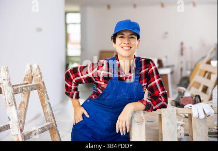 Jeune femme constructeur dans les vêtements de travail posant dans l'appartement pendant les travaux de réparation Banque D'Images