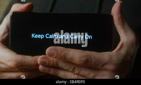 Personne tenant un smartphone avec éclairage Keep Calm et Carry on message dans l'obscurité Banque D'Images