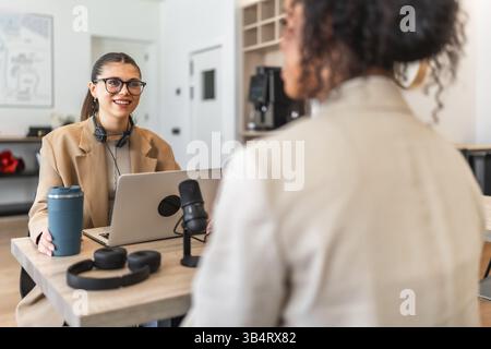 Deux podcasteurs enregistrent un nouvel épisode dans un bureau moderne à l'aide d'un ordinateur portable et d'un microphone professionnel Banque D'Images