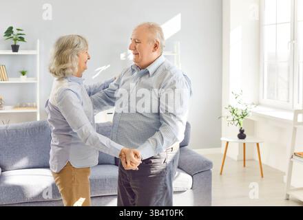 Heureux senior danse à la maison joyeux conjoints retraités mari et femme riant dansant dans le salon Banque D'Images