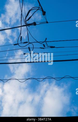 Des lignes électriques enchevêtrées contre un ciel bleu lumineux et des nuages blancs éparpillés Banque D'Images