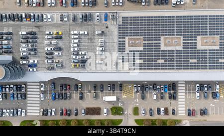 Vue aérienne d'un grand parking rempli de voitures, avec rangées et sections organisées. La partie supérieure montre un bâtiment avec des panneaux solaires sur la R Banque D'Images