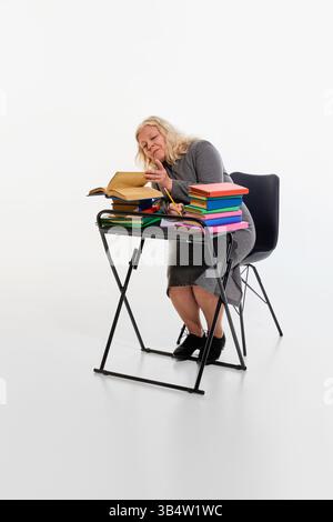 Surchargé avec l'étude. Femme âgée au bureau entourée de livres colorés sur fond blanc de studio, profondément axée sur la lecture, multitâche Banque D'Images