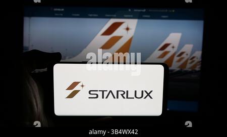 Dans cette illustration photo, une personne tient un téléphone portable avec le logo de la compagnie aérienne taïwanaise Starlux Airlines sur l'écran en face de la page Web. Banque D'Images