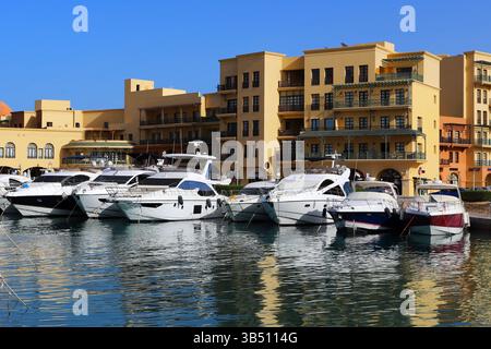 Yachts de luxe amarrés à une marina à El Gouna, en Égypte, avec un ciel bleu clair et des bâtiments en bord de mer reflétant dans l'eau calme de la mer Rouge. Banque D'Images