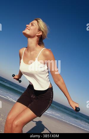 Jeune femme de formation de remise en forme avec des poids à la plage. Banque D'Images