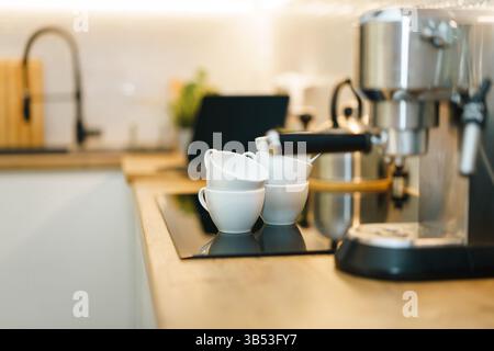 Gros plan machine à espresso élégante tasses blanches empilées sur le comptoir de cuisine moderne, avec fond d'ordinateur portable flou. L'image combine la télécommande confort maison Banque D'Images
