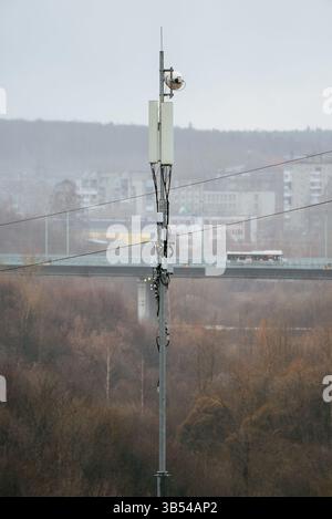 Tour de station de base cellulaire avec antennes et antenne parabolique à micro-ondes fournissant des services de communication sans fil dans un environnement urbain brumeux, avec un pont et des bâtiments en arrière-plan Banque D'Images