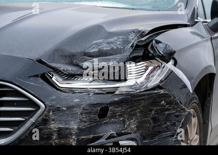 dommages importants à l'avant d'une voiture noire avec phare brisé et capot bosselé Banque D'Images