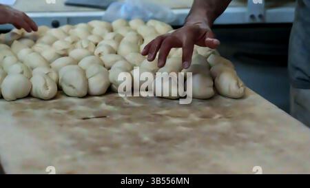 Gros plan de la main d'un boulanger façonnant soigneusement des portions de pâte sur une surface en bois farinée. L'image capture le processus artisanal de préparation du pain Banque D'Images