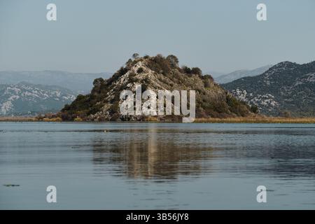Une vue imprenable sur les montagnes monténégrines luxuriantes et les rives recouvertes de roseaux du lac Skadar sous un ciel bleu clair, reflétant magnifiquement sur le reste wa Banque D'Images