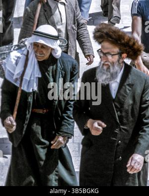 8 avril 1988, Jérusalem, Israël : un vieil homme juif israélien ultra orthodoxe (Haredi) barbu, portant un chapeau de fourrure rond traditionnel (shtreimel), et un homme palestinien âgé portant un keffiyeh traditionnel (couvre-tête) marchent côte à côte dans une foule à Jérusalem. (Crédit image : © Arnold Drapkin/ZUMA Press Wire) Banque D'Images