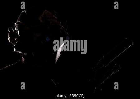 Un portrait frappant de silhouette d'une personne équipée d'une tenue tactique militaire et d'un équipement de vision nocturne high-tech, debout dans le foreg ombragé Banque D'Images