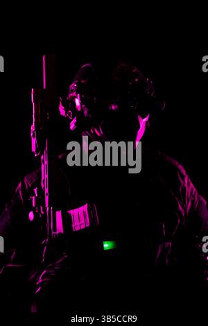Une photographie artistique en basse lumière d'un soldat dans des équipements tactiques et des armes de haute technologie, soulignée par un éclairage rose et vert éclairant les détails clés, Banque D'Images