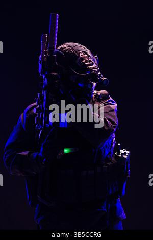 Un opérateur tactique vêtu d'un équipement équipé de lunettes de vision nocturne et d'une arme à feu perfectionnée, représentée dans un éclairage artistique, représentant la force, Banque D'Images