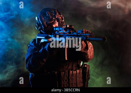 Un soldat tactique en pleine vitesse vise une arme au milieu d'un éclairage spectaculaire et d'une fumée colorée, exsudant intensité et concentration. L'image représente l'intensité, s. Banque D'Images