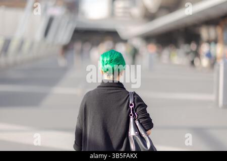 Vue arrière de la femme aux cheveux verts marchant dans un cadre urbain gris - Pop de couleur Banque D'Images