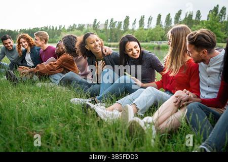 Groupe diversifié de jeunes amis assis ensemble à l'extérieur, profitant d'un moment détendu de liaison et de connexion authentique dans la nature. Banque D'Images