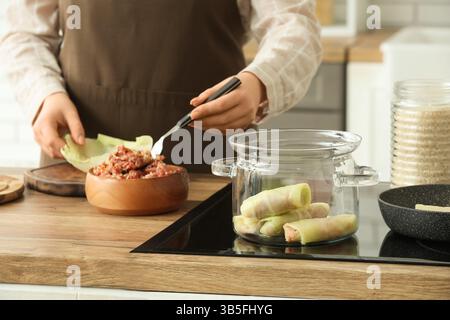 Casserole de cuisson avec des rouleaux de chou farcis contre la femme cuisinant à table dans la cuisine, gros plan Banque D'Images