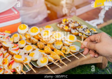 Oeufs de caille frits dans des brochettes de bambou sur la main de la femme, servir chaud avec du sel et du poivre moulu. Apéritif thaïlandais au marché alimentaire de rue. Banque D'Images