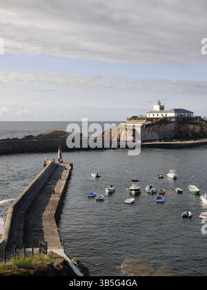 Bateaux flottant près de la jetée en béton menant au phare sur l'îlot par jour nuageux à tapia de casariego, asturies, espagne Banque D'Images