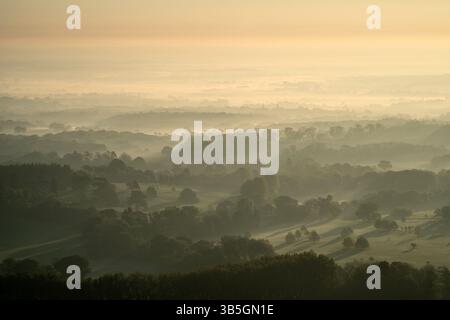 Vue depuis Chanctonbury Hill, South Downs, West Sussex, Royaume-Uni au lever du soleil le 1er mai alors que la brume brûle sur le paysage ci-dessous. Banque D'Images