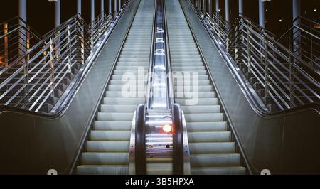 Angle bas et vue rapprochée sur un long escalier roulant dans un bâtiment public. scène nocturne Banque D'Images