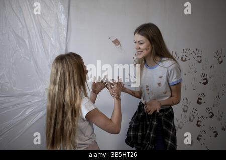 Deux jeunes femmes s'engagent joyeusement dans une interaction ludique, sur fond coloré et désordonné, plein d'énergie Banque D'Images