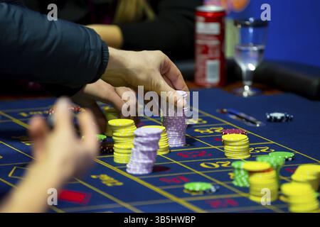 Table de roulette avec des mains humaines déposant des jetons dans le casino. Roue de roulette au premier plan. Jeu de pari. Des gens méconnaissables Banque D'Images